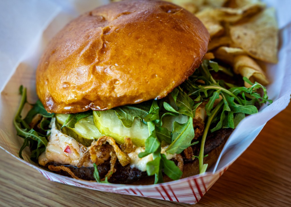 Close-up of cheeseburger with pickles, arugula, and crispy onions
